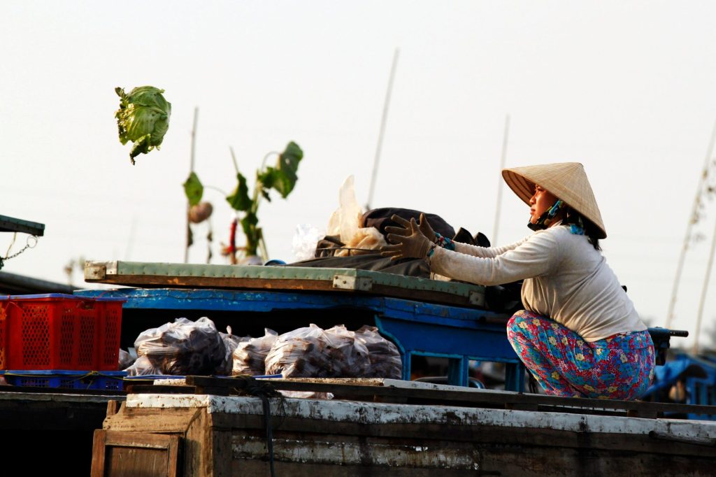 A vendor selling from a wooden boat along a Ben Tre coconut-palm canal